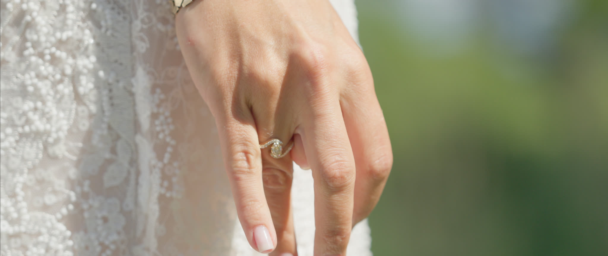 Nærbillede af brudens hånd med forlovelsesring mod blondekjolen